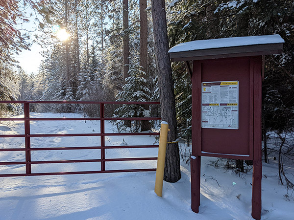 A kiosk at a forest entrance that is blocked by a gate