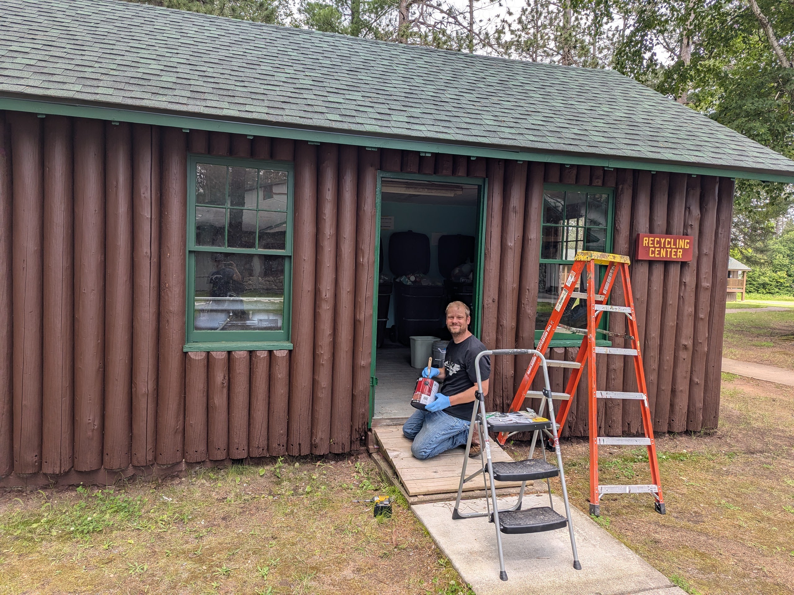 man kneeling and painting inside doorway of shed 