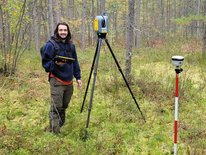 student standing next to tripod in the woods